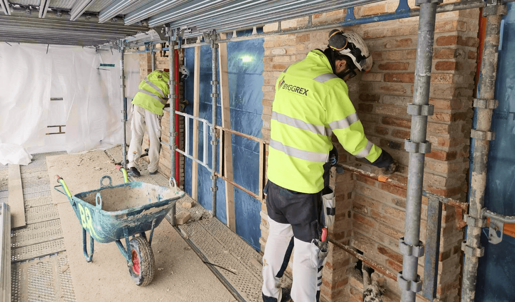 Två män på ställning utför fasadarbete