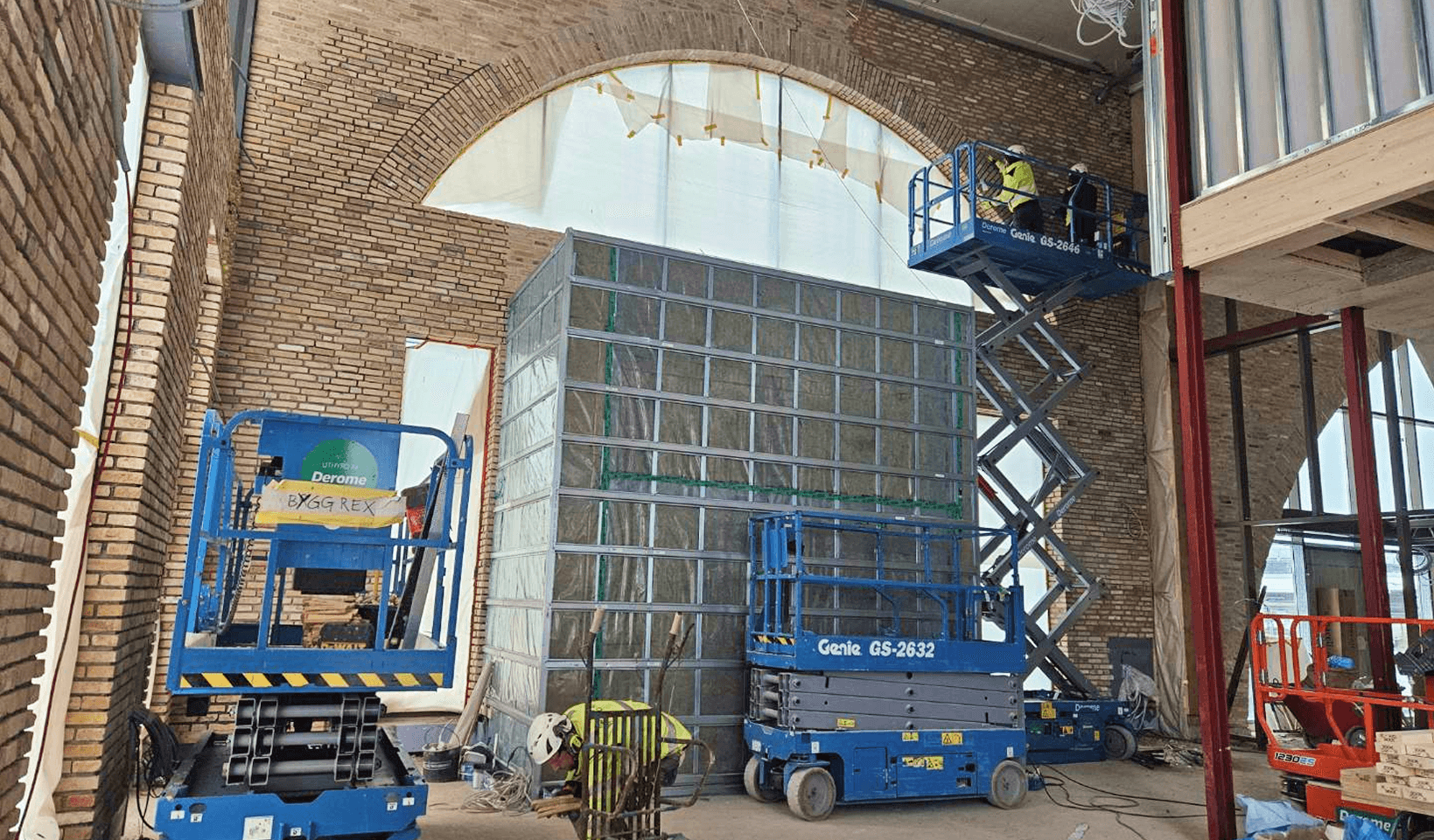 Två män i en saxlift utför arbete på insidan av fasaden