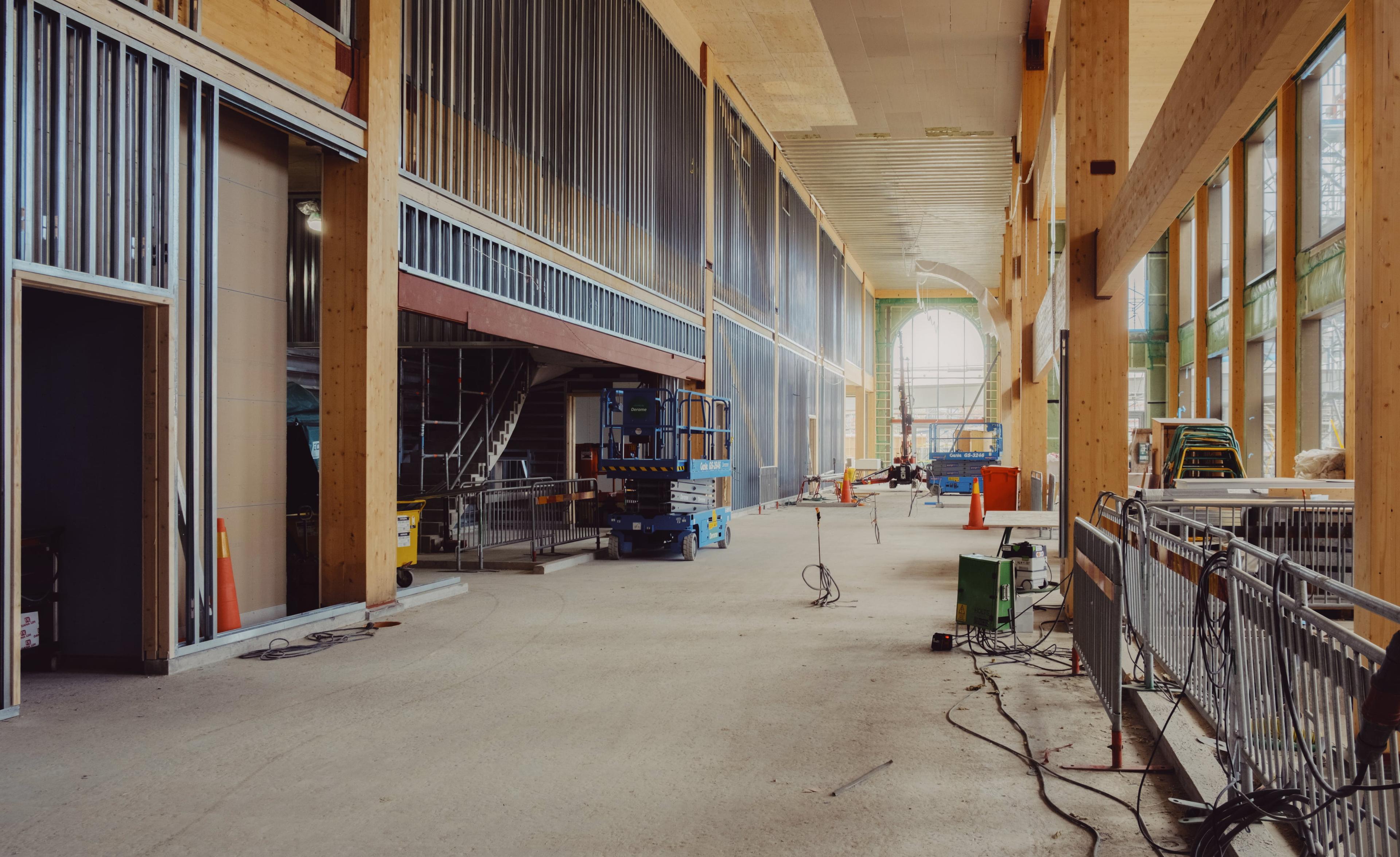 Interiör av stationshallen under byggfasen med synliga träbalkar, metallräcken och byggmaskiner på golvet