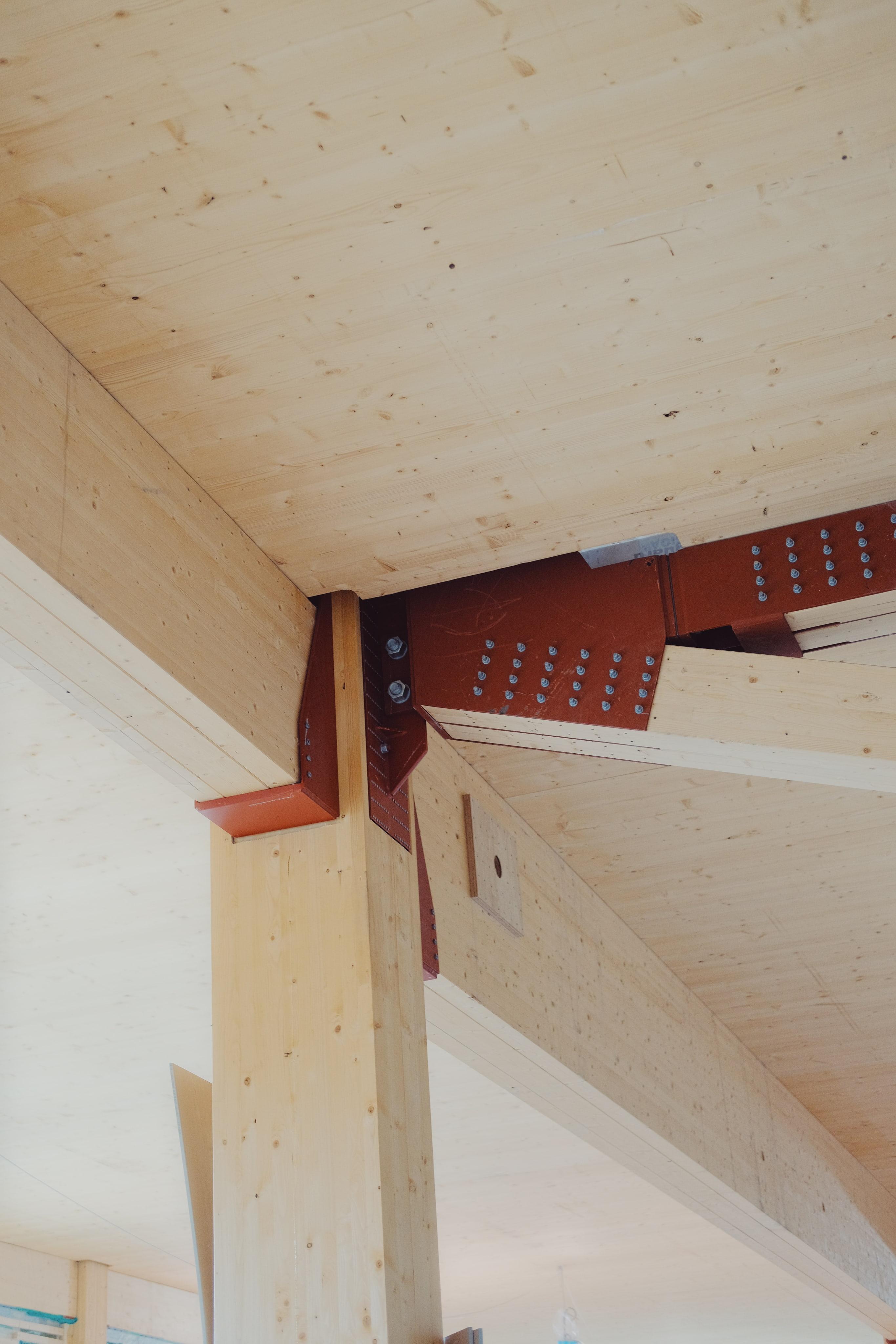 Närbildsvy av träbalkars sammanfogning med röda metallplattor och bultar i limträkonstruktionen
