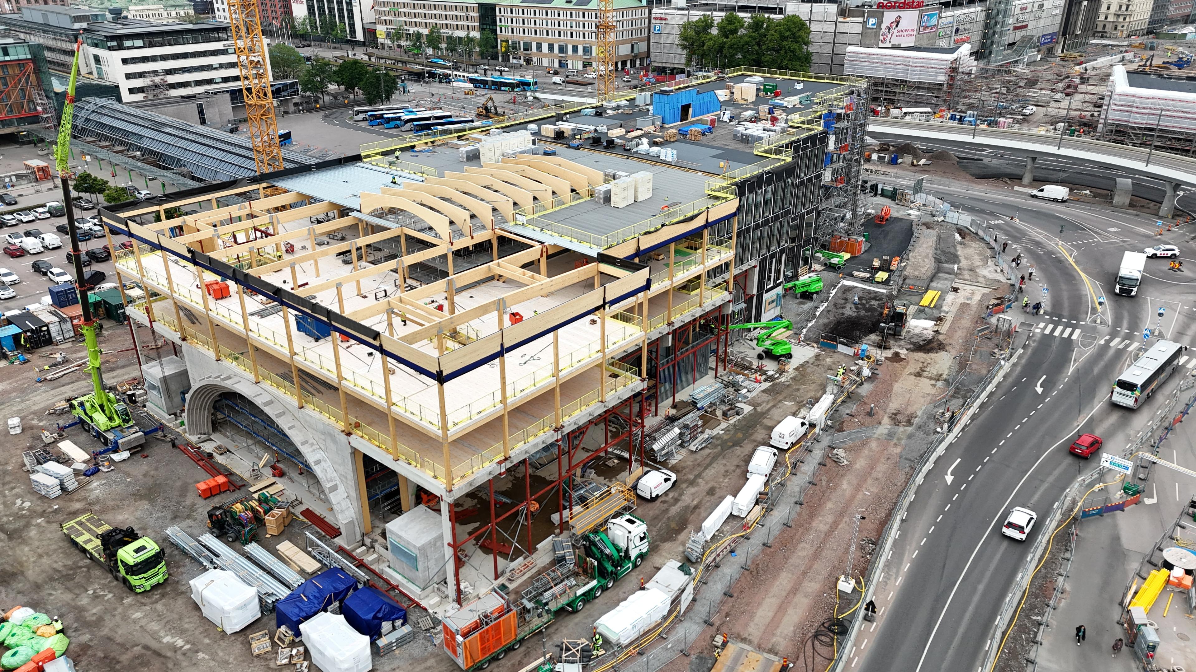 Flygfoto över byggarbetsplatsen för Göteborg Grand Central med synliga träkonstruktioner, kranar, byggmaskiner och omgivande stadstrafik