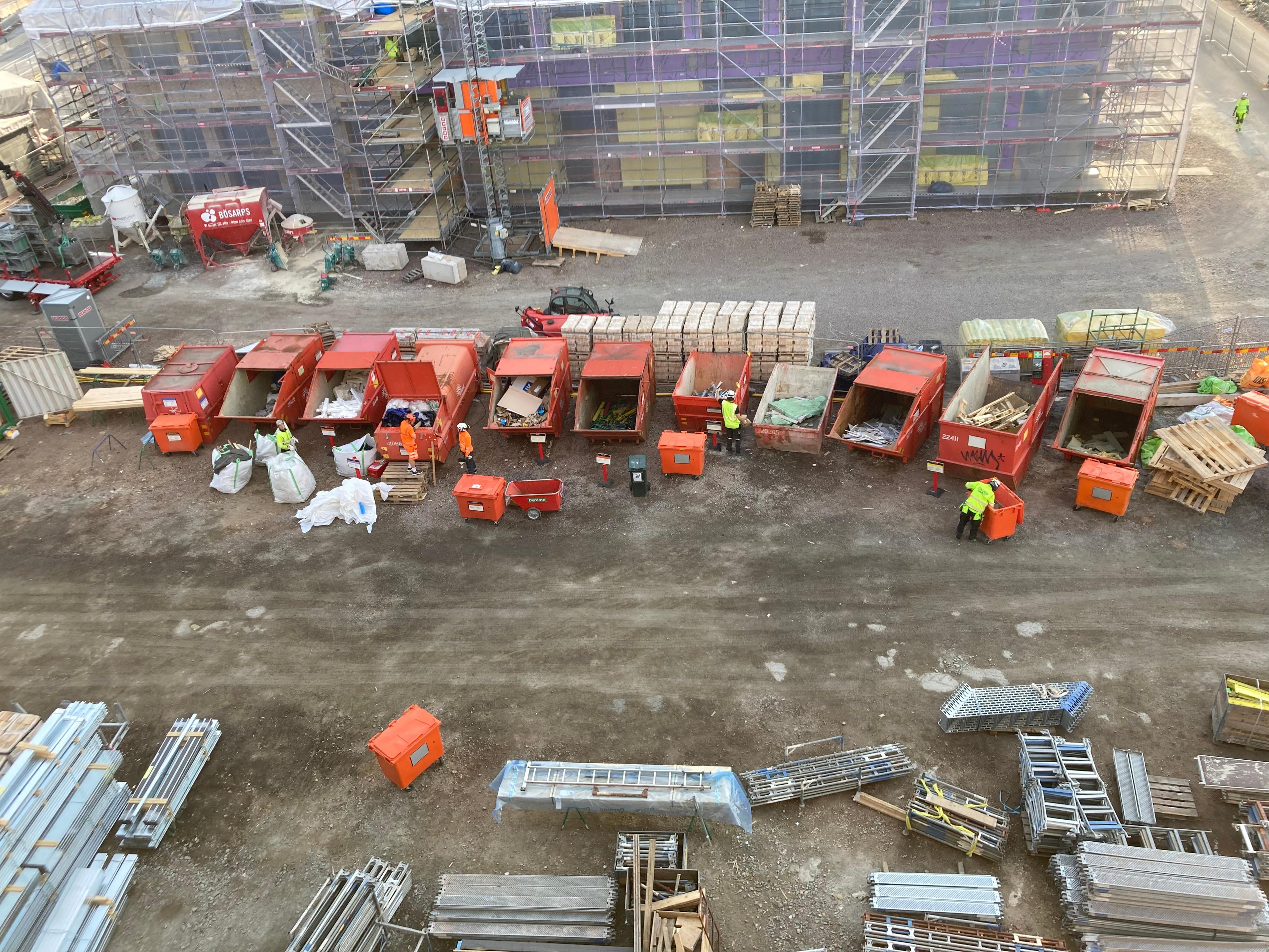 Flygvy över välorganiserade rader av orange avfallscontainrar och sorterat byggmaterial som resultat av gemensamma städinsatser