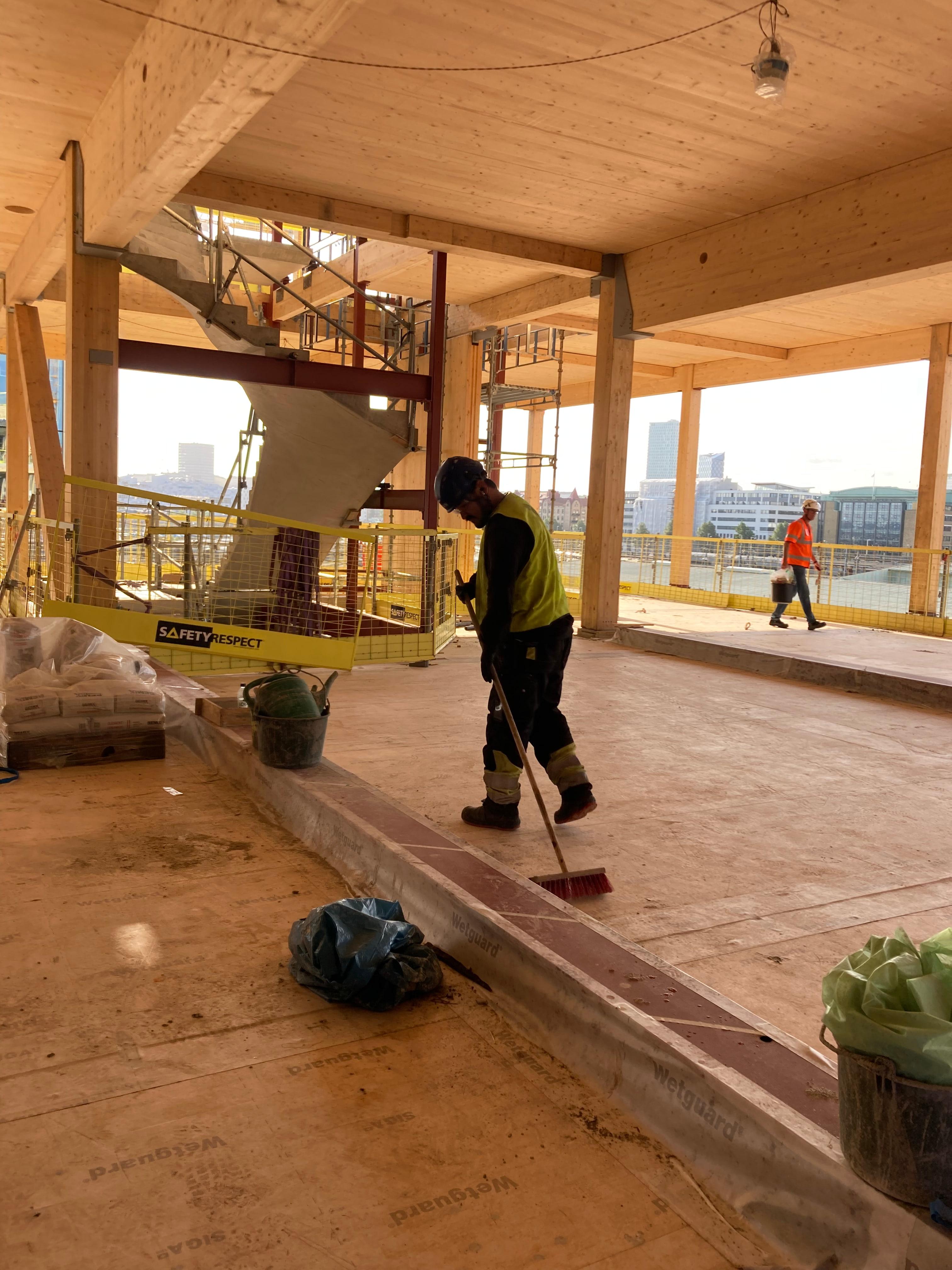 Byggarbetare sopar rent golvet i träkonstruktionen med limträbalkar