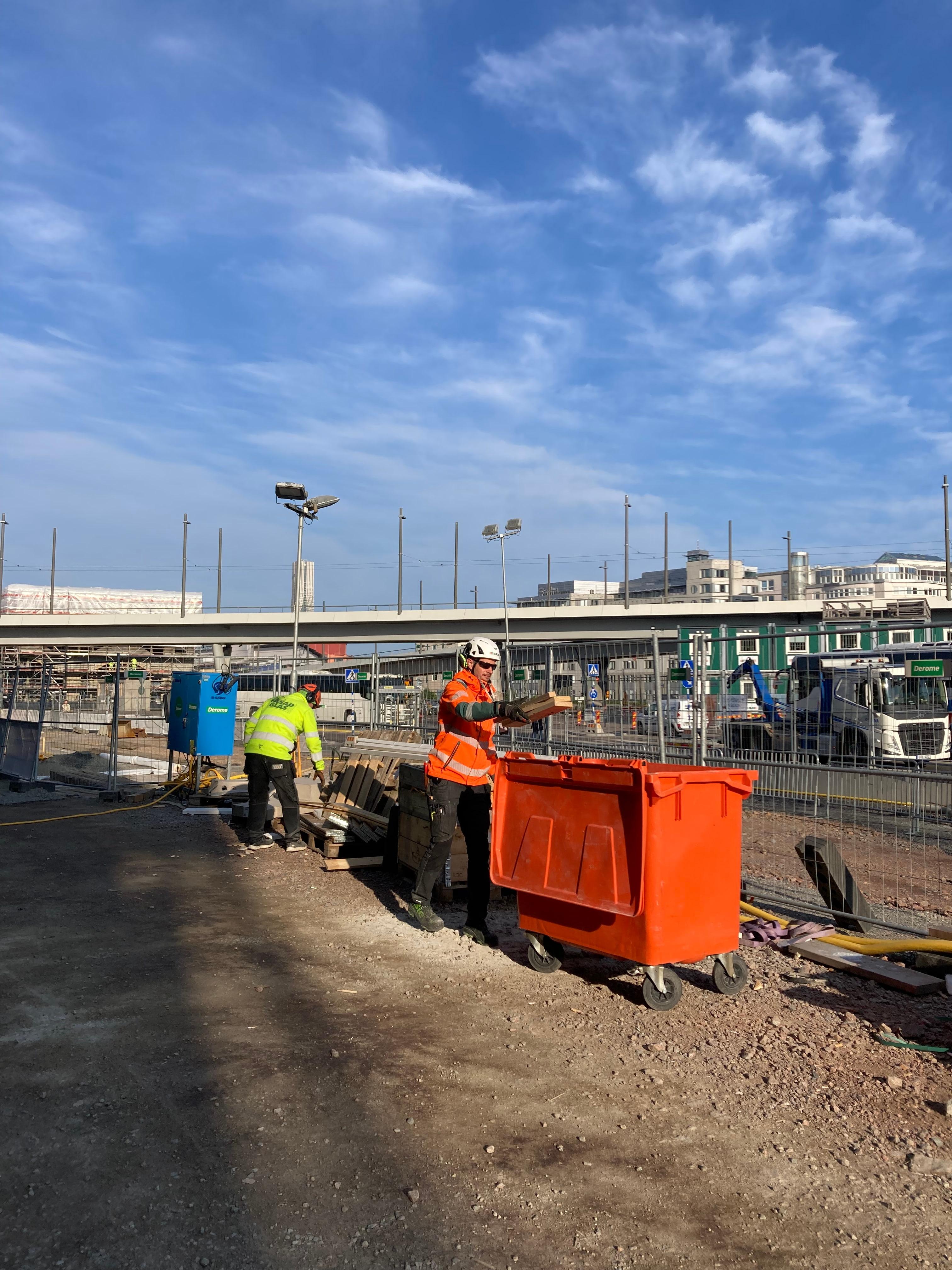 Byggarbetare i säkerhetsvästar deltar i den veckovisa städdagen och organiserar material på byggarbetsplatsen