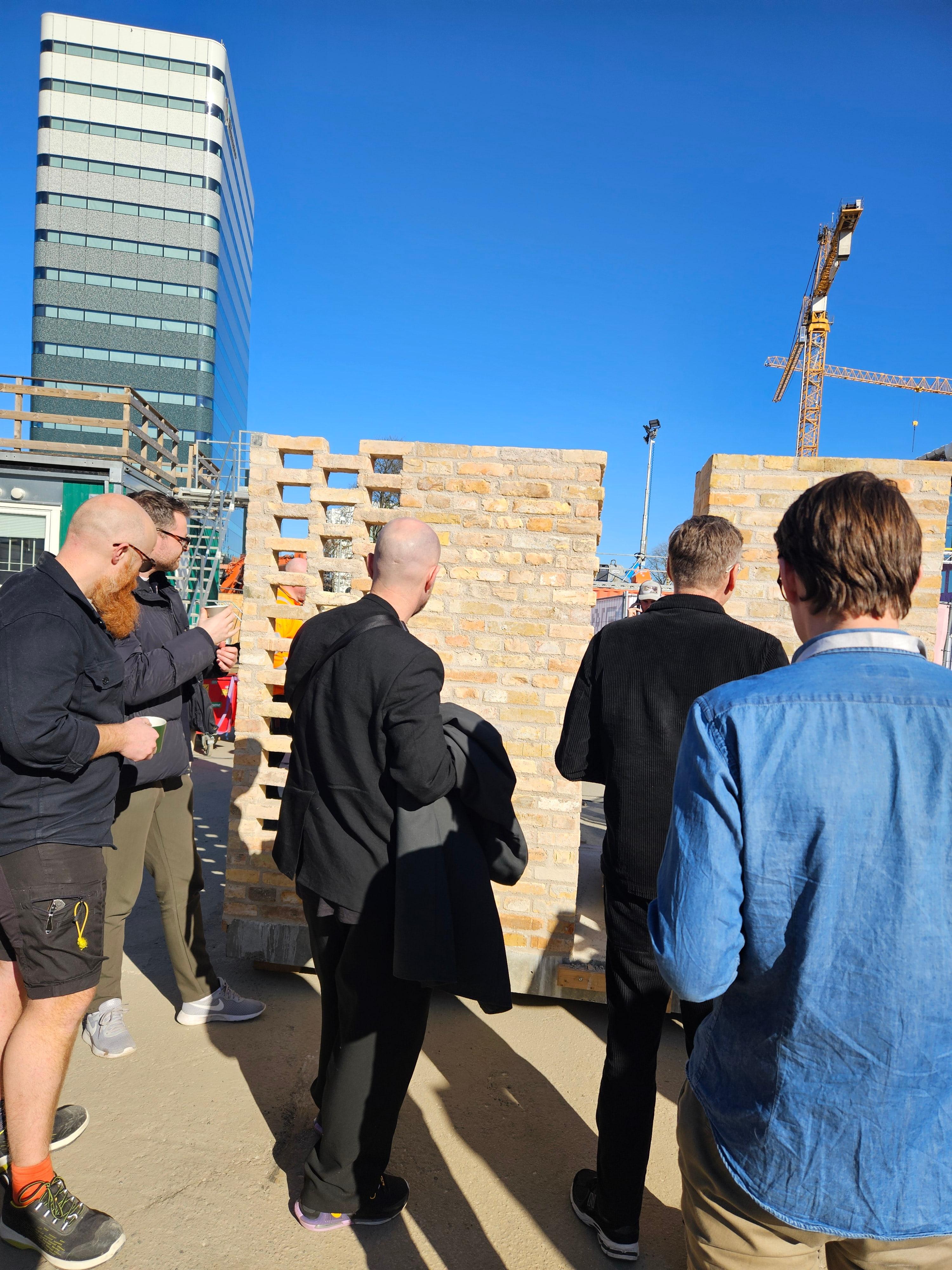 Grupp med män och byggkläder studerar tegelprover på byggarbetsplatsen med tegelväggar