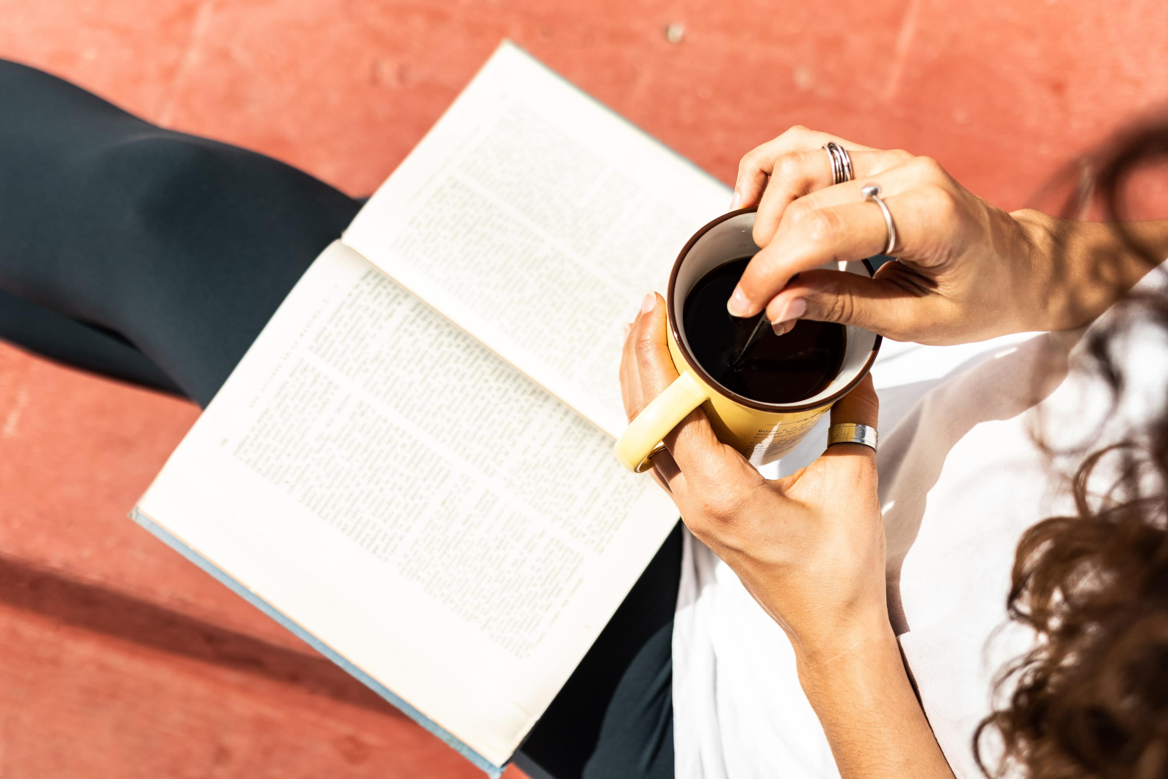 Sittande person som håller en kaffekopp och läser en bok